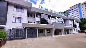 Un hôtel appelé « Olive Gardens Hotel », doté d’une architecture moderne, comprenant plusieurs étages et un vaste hall d’entrée.