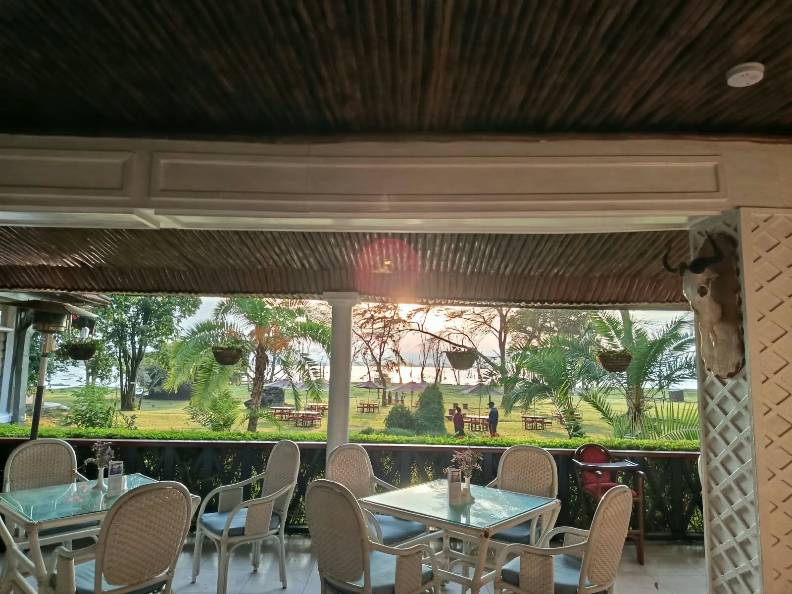 An outdoor seating area with tables and chairs, overlooking a landscaped garden and a body of water.