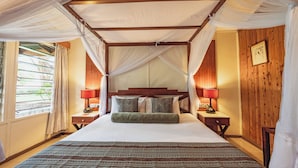 A four-poster canopy bed with a wooden headboard, two bedside lamps, and a view of the outdoors through a window.