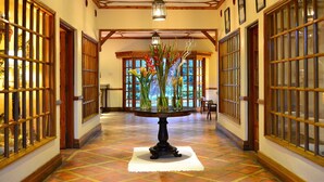 A hallway with a round table in the center, flanked by wooden-framed windows and doors.