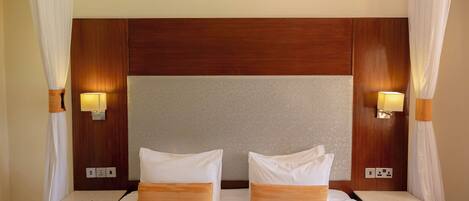 A hotel room with a large bed, two bedside tables, a wooden headboard, and wall-mounted lamps.