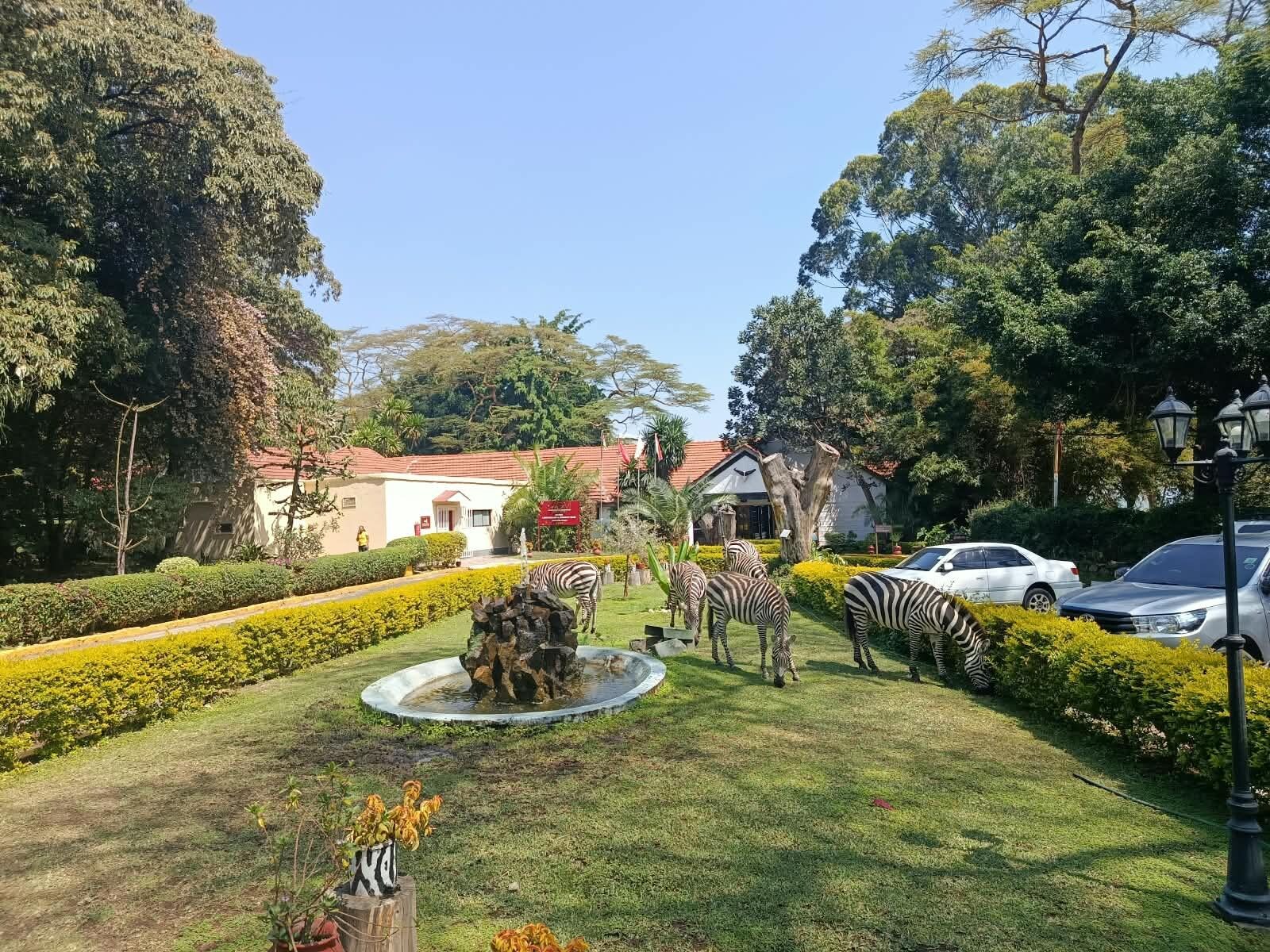 Ein gepflegter Garten mit Brunnen, Hecken und einem Gebäude mit rotem Dach.