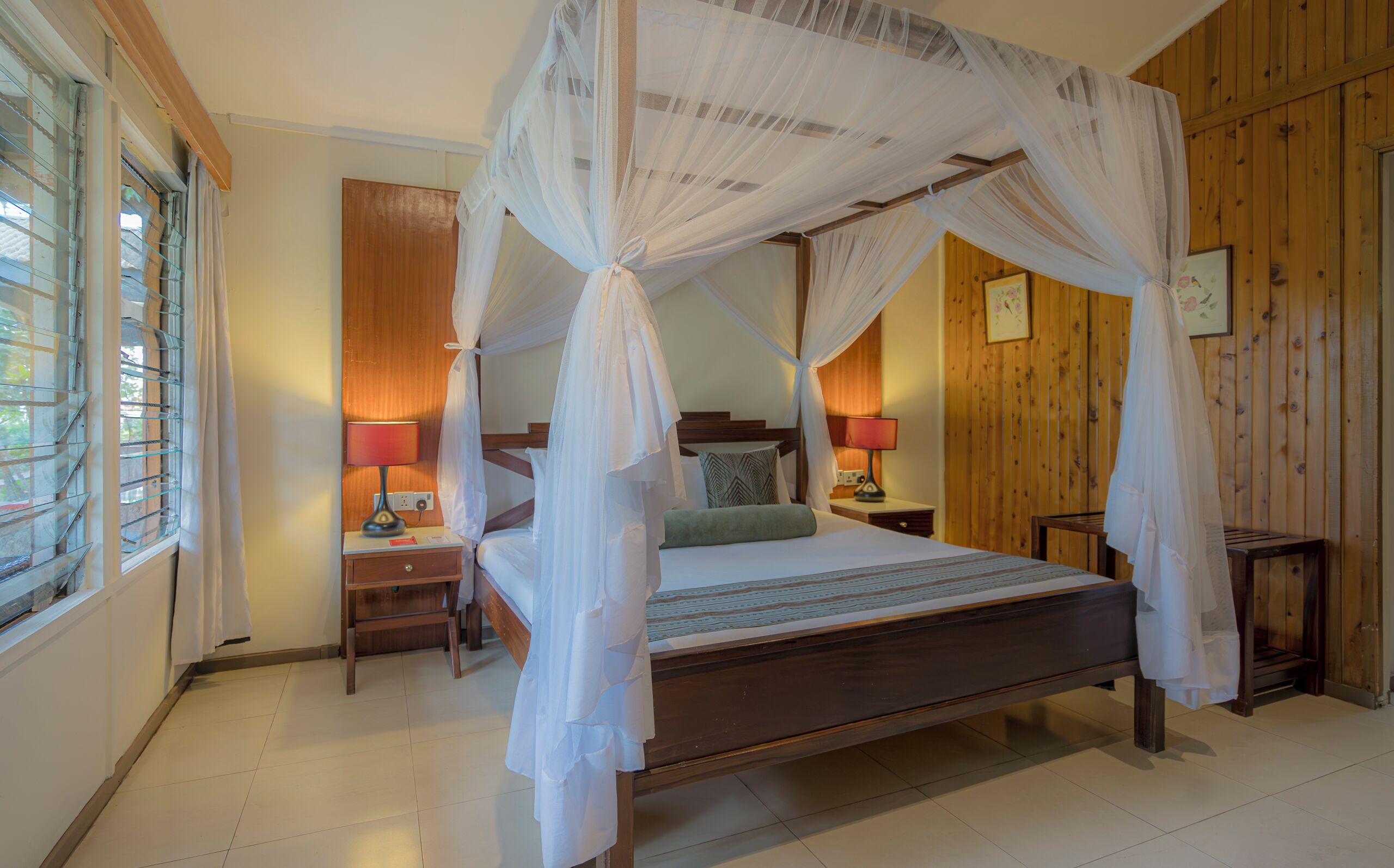 A four-poster bed with a canopy, bedside lamps, a wooden nightstand, and a wooden wall panel.