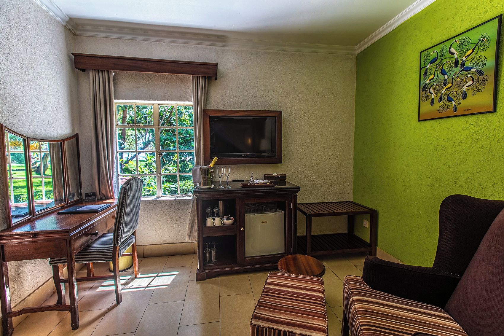 Habitación con televisión, escritorio, silla, sofá y ventana con cortinas.