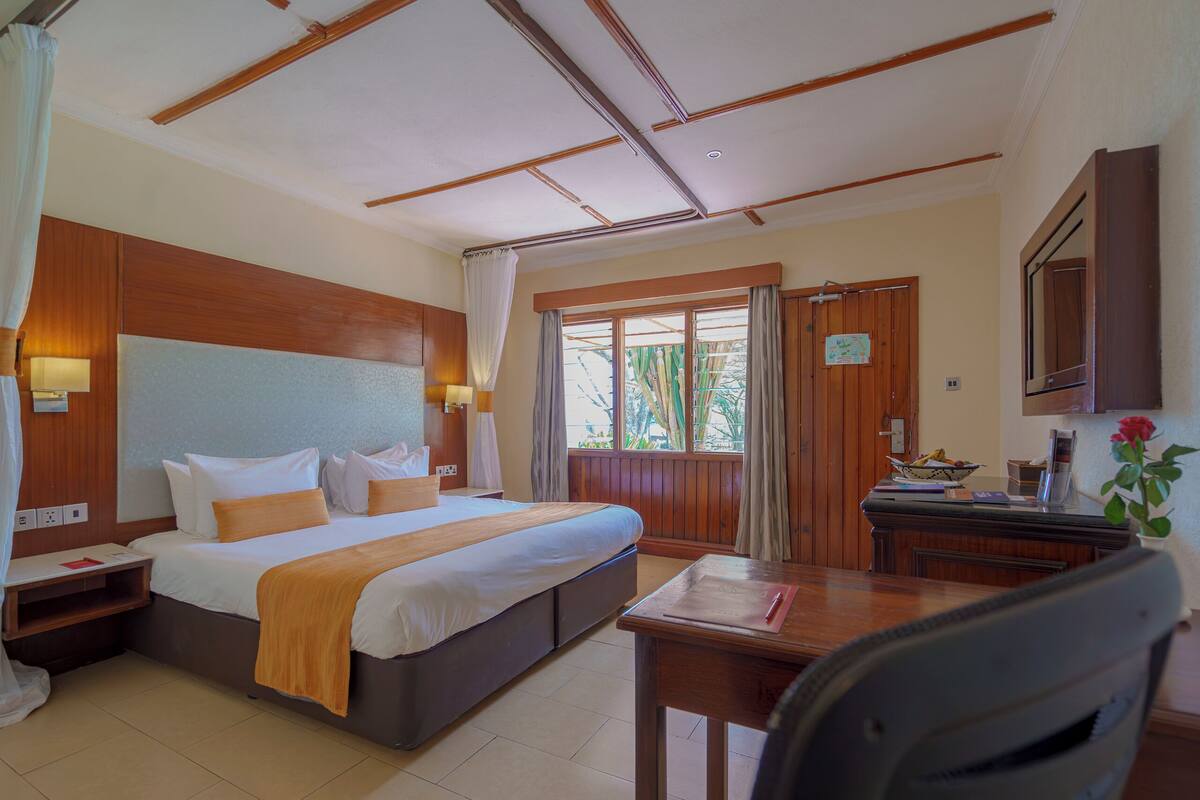 Ein Hotelzimmer mit einem großen Bett, einem Schreibtisch, einem Stuhl und einem fenster mit Vorhängen.