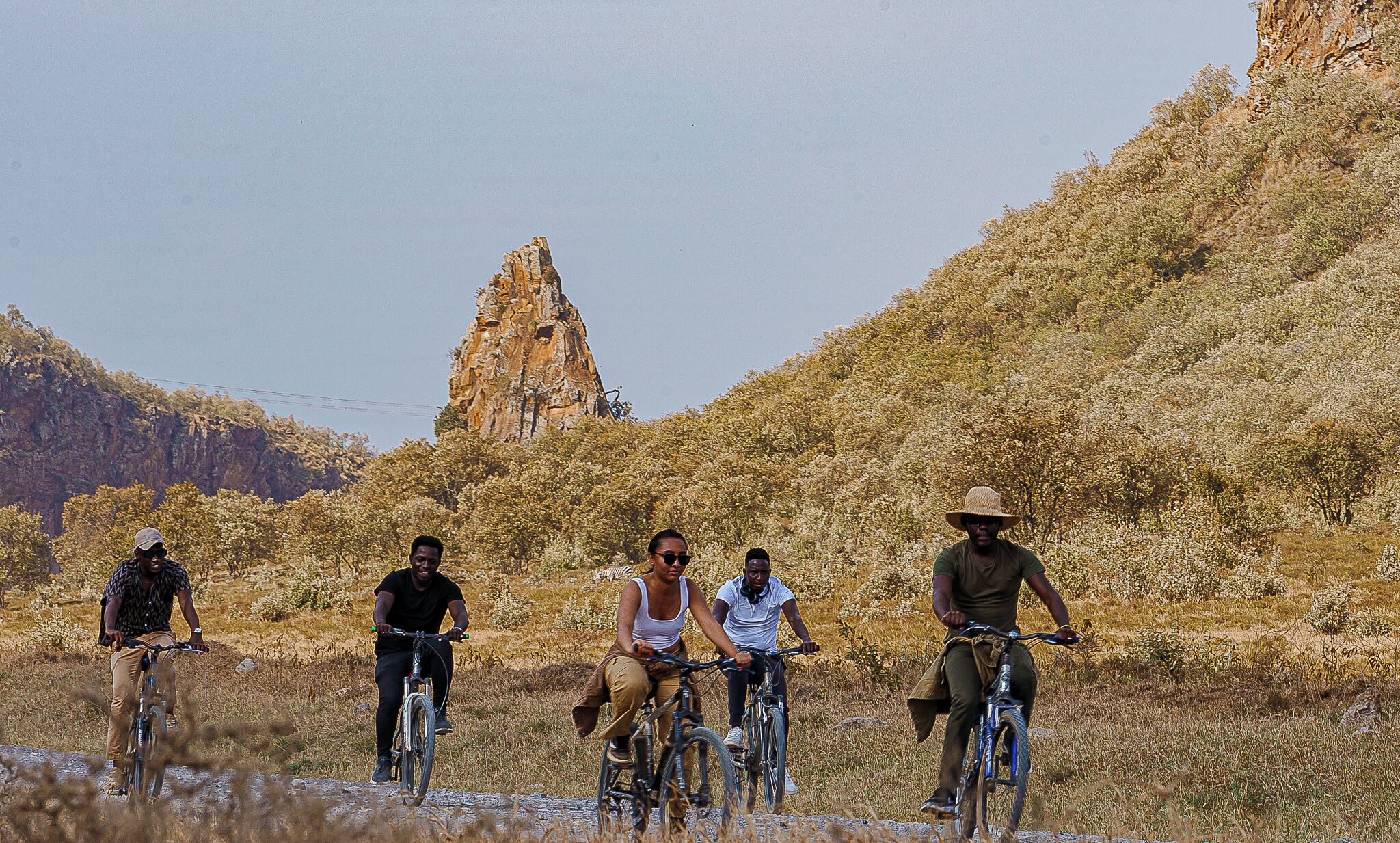 Un grupo de personas andando en bicicleta por un camino rural, con una colina rocosa y vegetación escasa al fondo.