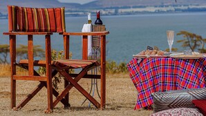 A wooden chair and table set up by a lake with a view of mountains in the background.