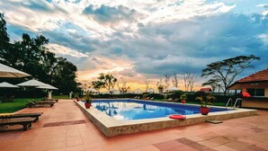 A swimming pool with lounge chairs and umbrellas, surrounded by a tiled patio and trees.