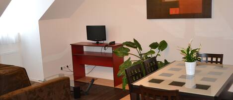 Un comedor moderno con una mesa, sillas, un televisor sobre un soporte y una planta en maceta.