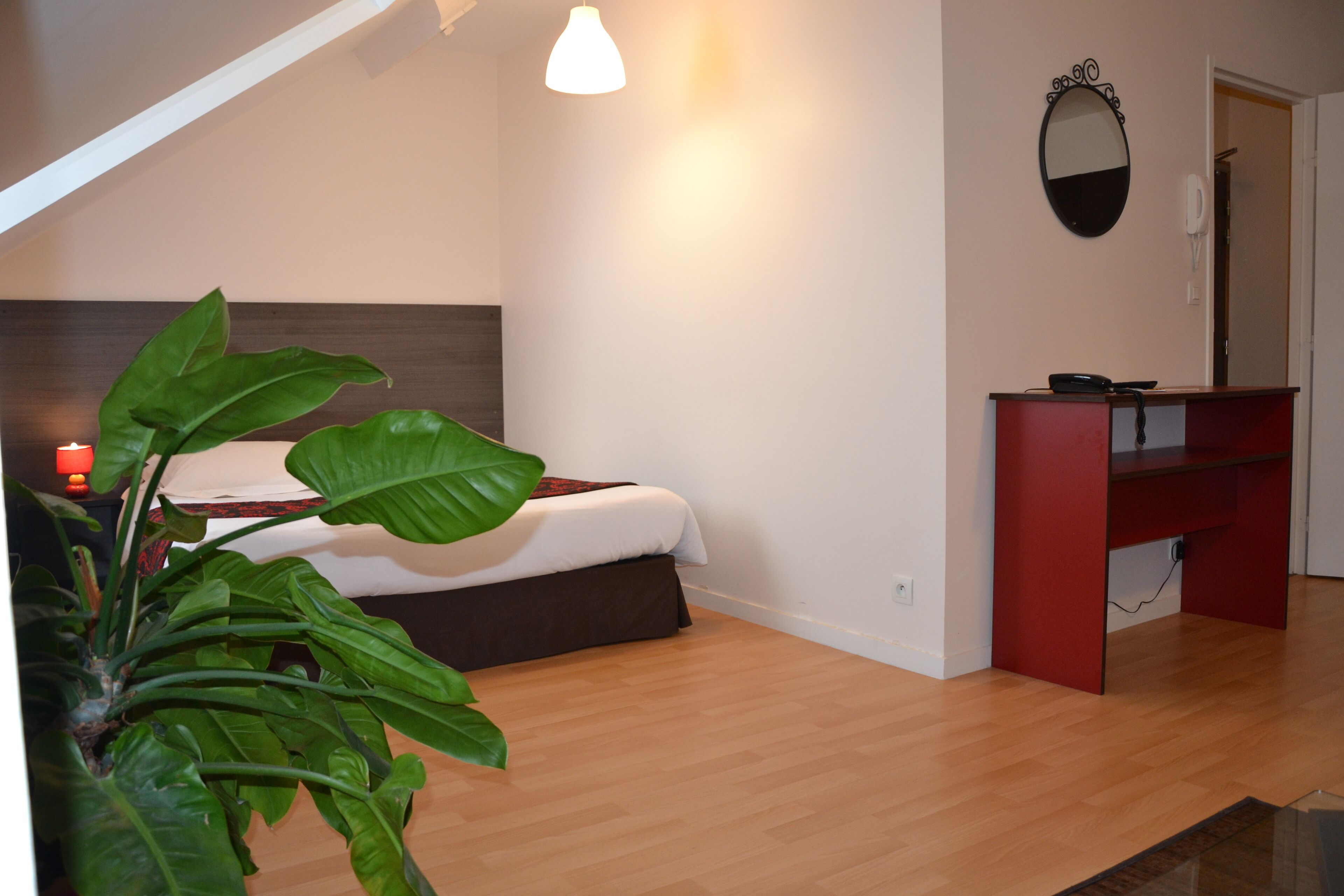 A bedroom with a bed, a desk, a mirror, and a plant.