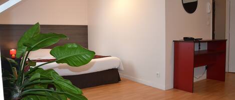 A bedroom with a bed, a desk, a mirror, and a plant.