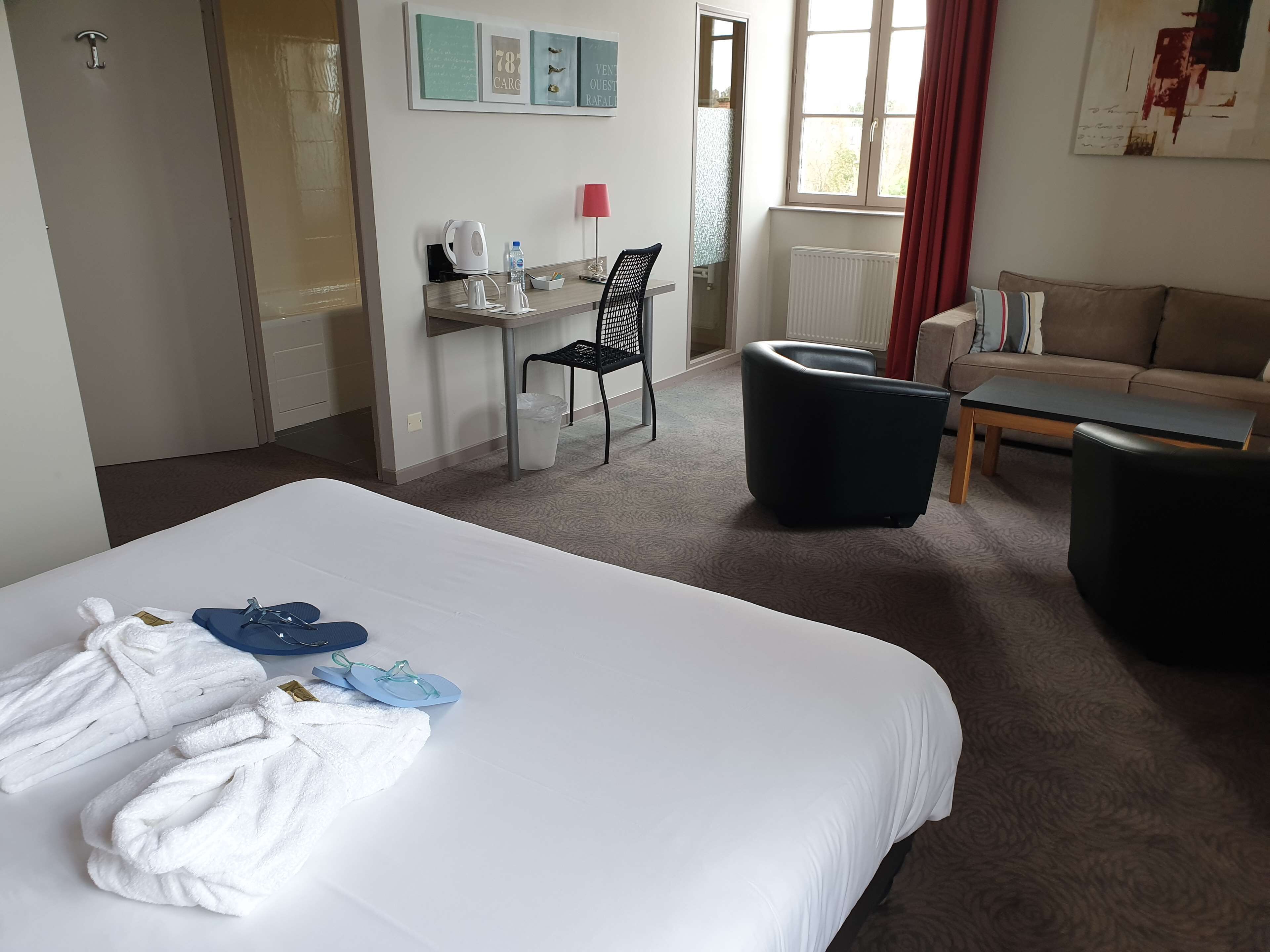 Una habitación de hotel con una cama grande, un escritorio con silla, un sofá y una ventana con cortinas.