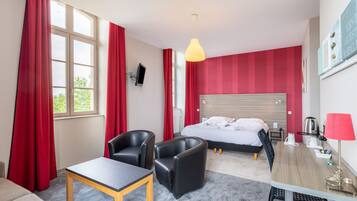 A hotel room with a bed, two chairs, a table, a desk, a lamp, and a TV.