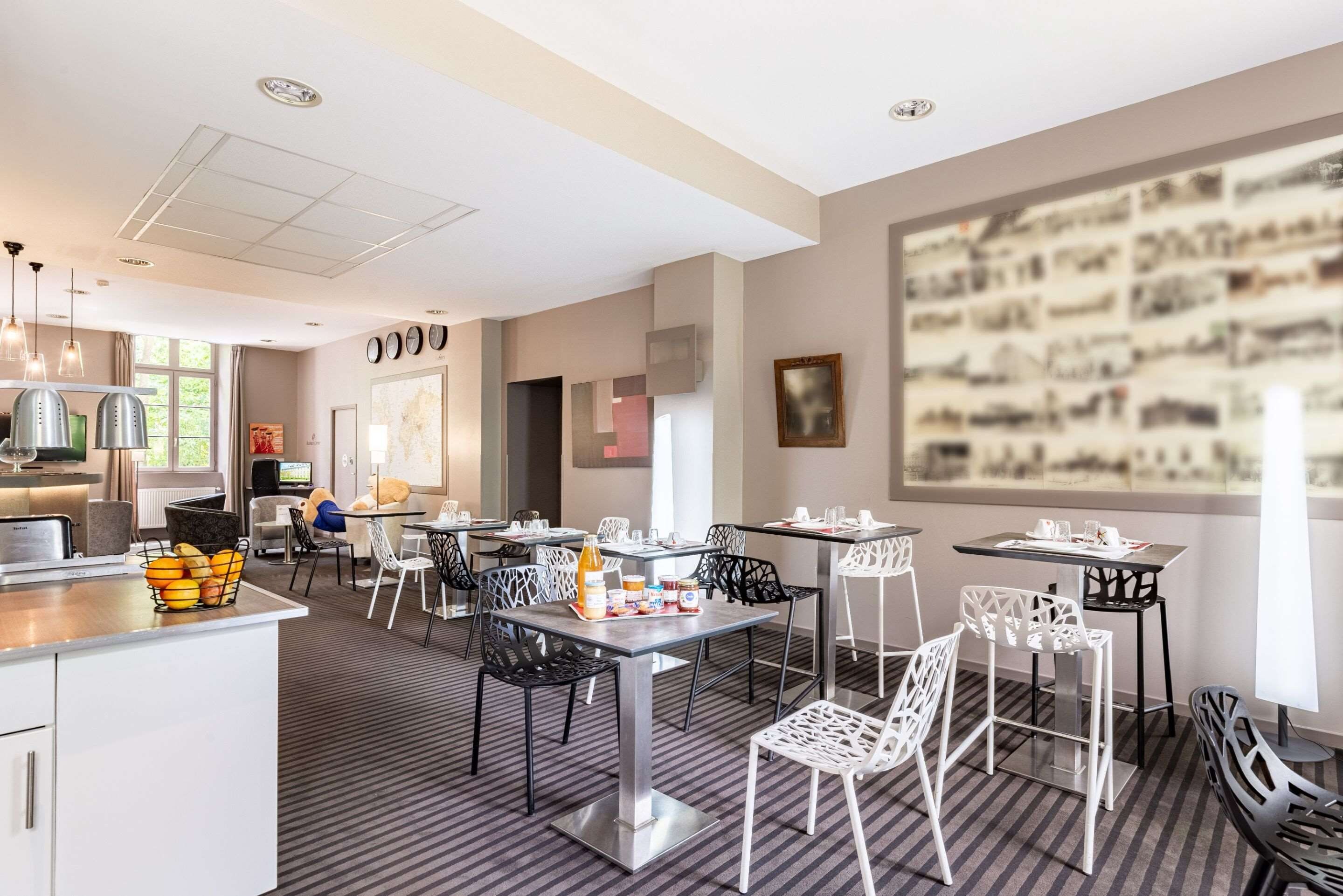 A modern dining area with tables and chairs, a kitchen area with appliances, and a large wall with a collage of images.