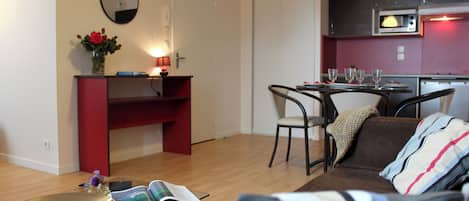 Un salon moderne avec un canapé, une petite table et un meuble rouge. Il y a également un coin cuisine avec un four à micro-ondes et une table à manger avec des chaises.