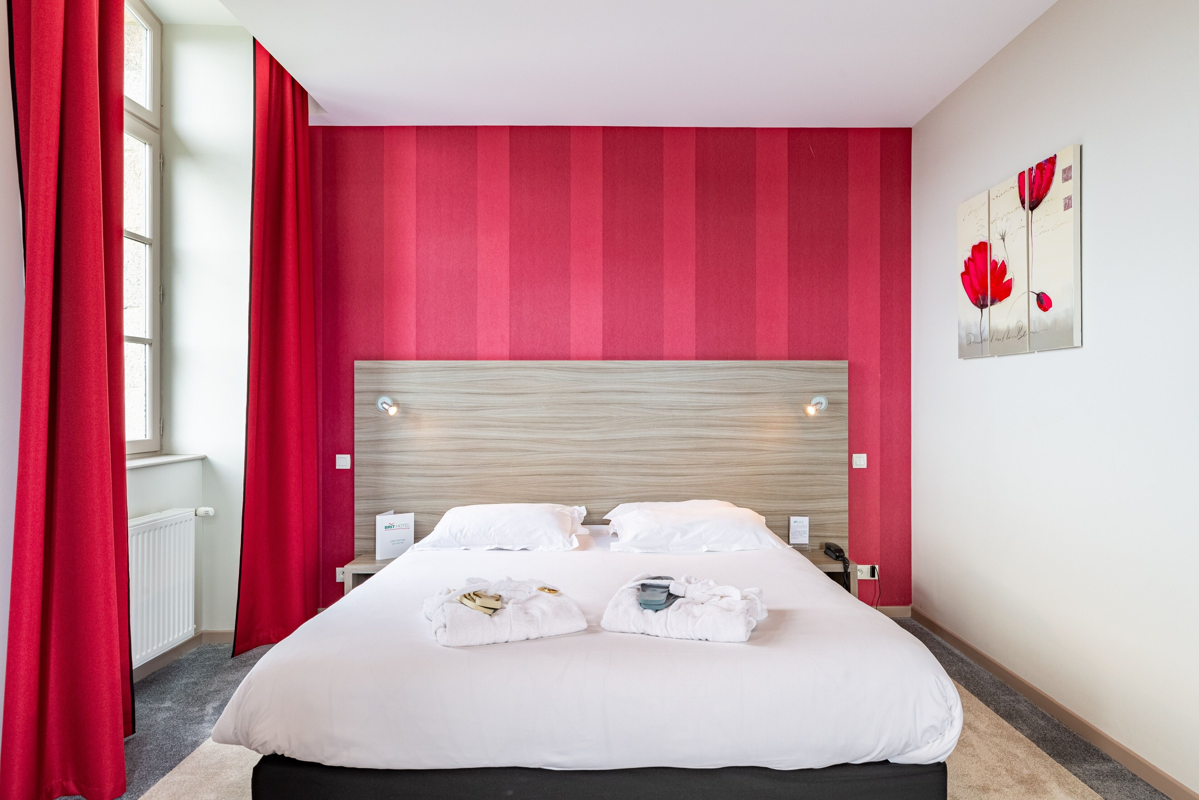 Habitación de hotel con una cama grande, cortinas rojas, cabecero de madera y un cuadro en la pared.