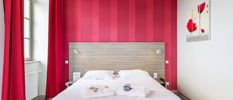 A hotel room with a large bed, red curtains, a wooden headboard, and a painting on the wall.