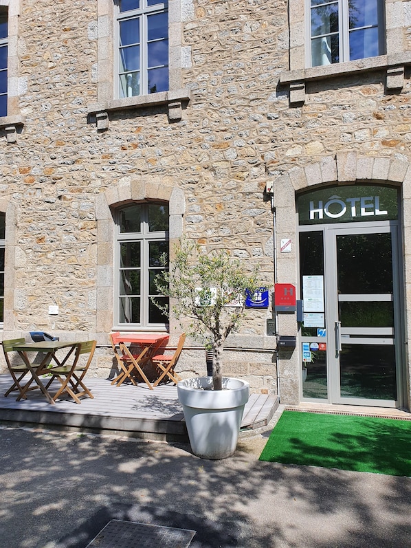 A stone building with a sign reading "HOTEL" above the entrance. There are outdoor tables and chairs, and a large potted plant in front. - Brit Hotel Dinan Le Connetable (Dinan)