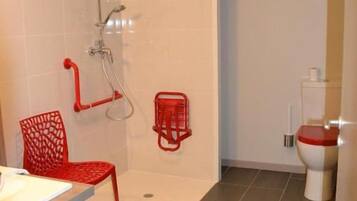 Ein Badezimmer mit Dusche, Toilette und einem roten Stuhl.