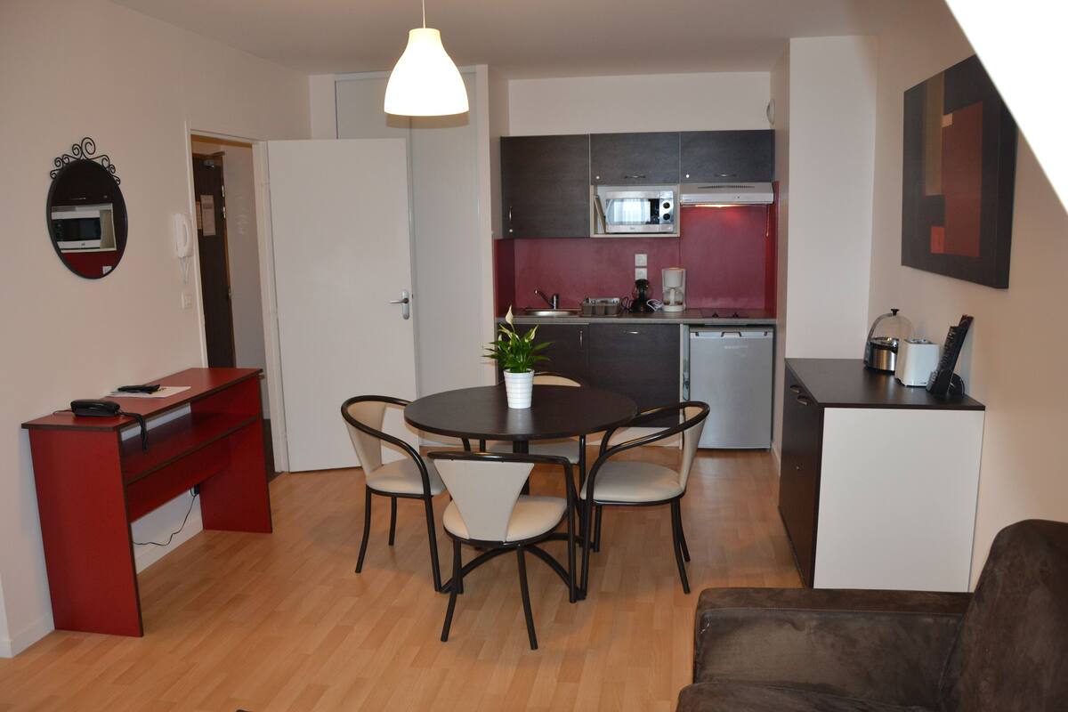 A compact living space with a dining area, kitchenette, and a small office desk.