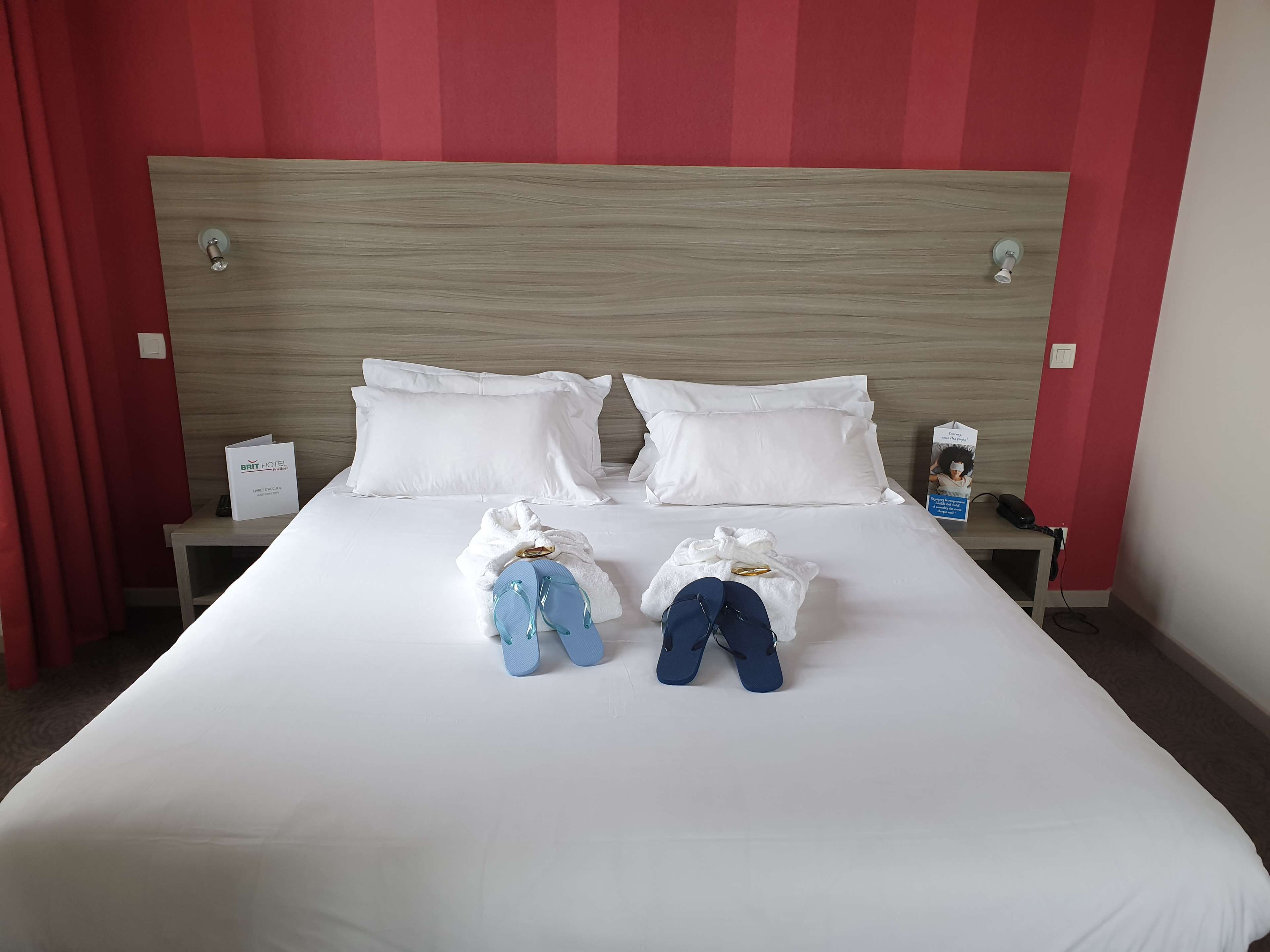 A neatly made bed with white bedding, two pillows, and a sign indicating it's a BRIT HOTEL room.