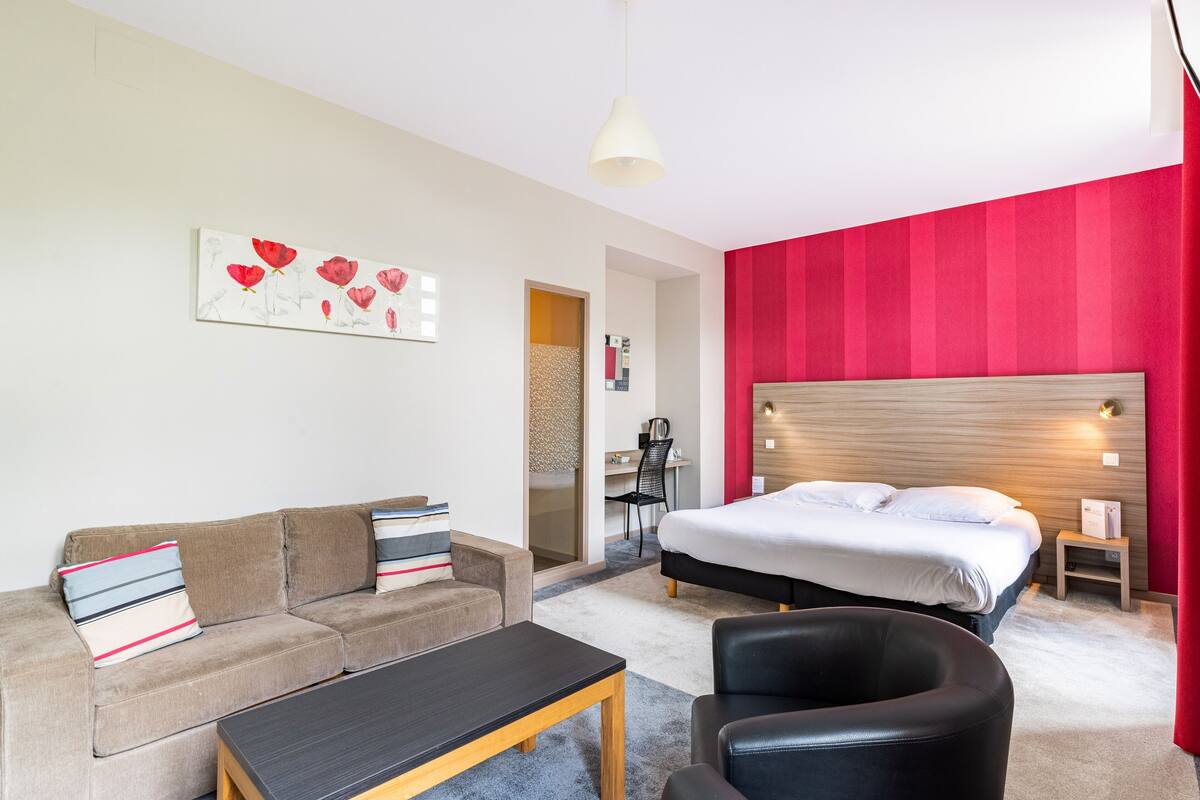 A modern hotel room with a bed, a sofa, a coffee table, and a desk.