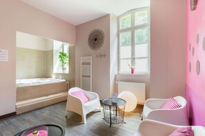 Habitación con bañera, dos sillas, una mesita, un radiador y una ventana con vistas.