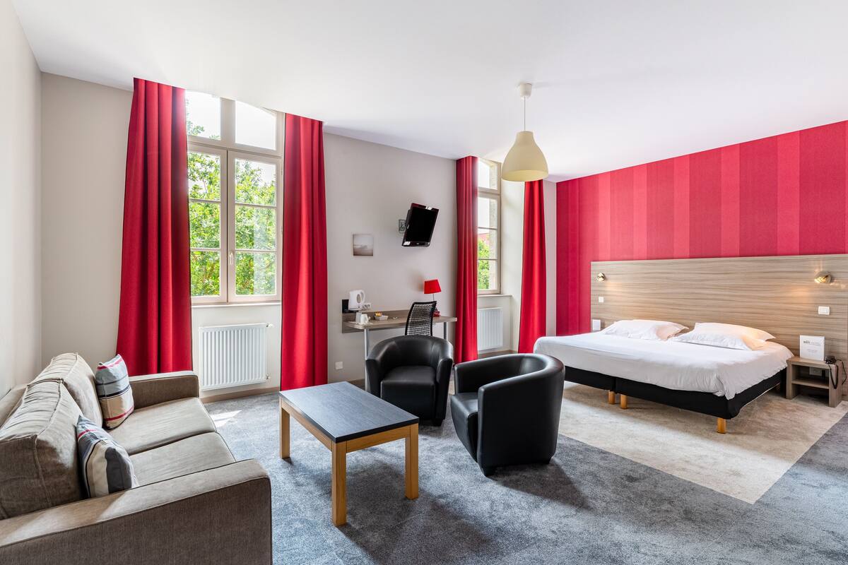 A hotel room with a bed, a desk, a chair, a sofa, and a table.