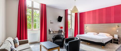 A hotel room with a bed, a desk, a chair, a sofa, and a table.