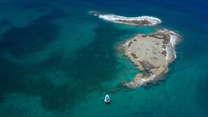 An aerial view of a small island with clear turquoise waters, rocky shoreline, and a boat anchored near the shore. - Dolphin Village - Sea Resort (Mateh Asher)