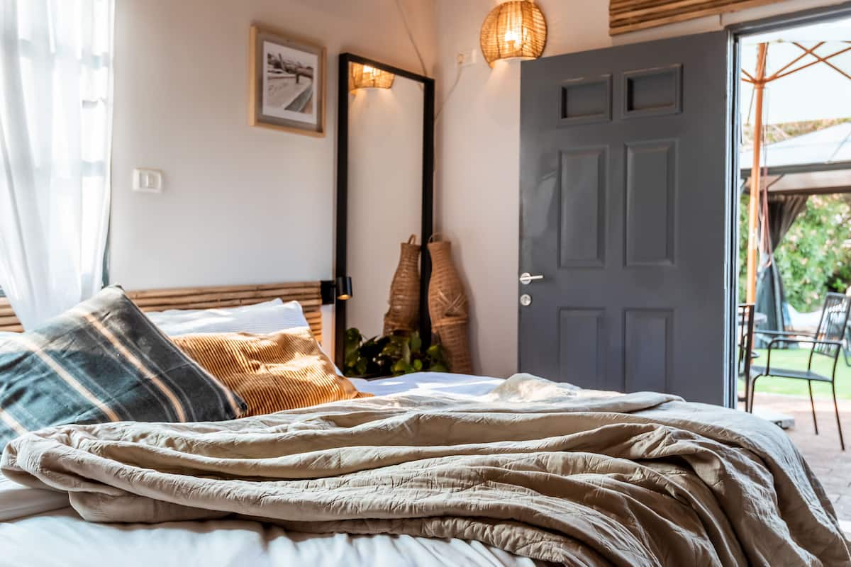 A neatly made bed with a beige blanket and pillows, a large mirror, and a door leading to an outdoor area.