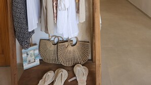 A clothing rack with various garments and accessories, a wooden display shelf with woven bags and slippers, and a hallway with decorative wall mirrors. - Dolphin Village - Sea Resort (Mateh Asher)