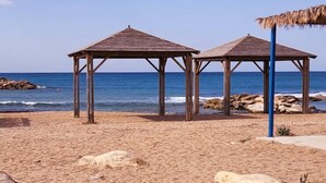Two wooden beach shelters with thatched roofs on a sandy beach with the ocean in the background. - Dolphin Village - Sea Resort (Mateh Asher)