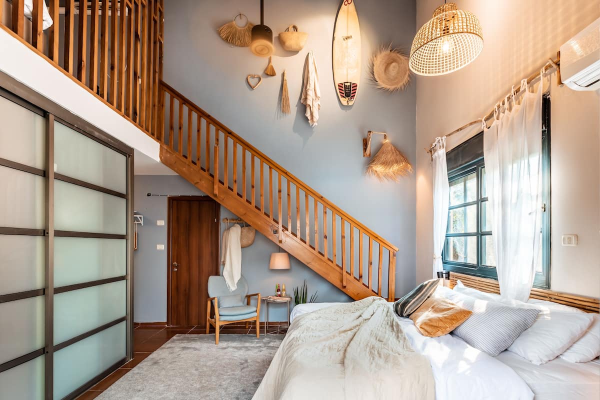 A bedroom with a large bed, a wooden staircase, and a view of the outdoors.