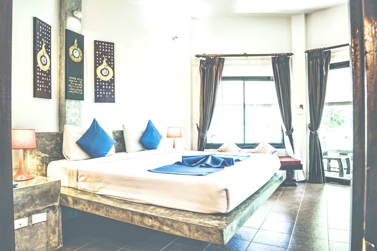 Une chambre d’hôtel avec un grand lit, une table de chevet, une lampe et une vue sur l’extérieur par une fenêtre munie de rideaux.