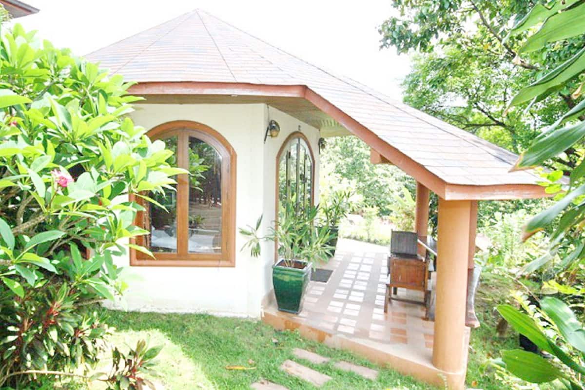 Une petite maison avec un porche carrelé, une porte en bois et une fenêtre.