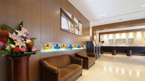 A reception area with a sofa, a vase of flowers, and a display of colorful glass vases. - Hotel Hokke Club Osaka (Osaka)