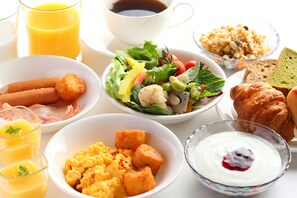 Taula de l'esmorzar amb diferents plats, com ara ous barrejats, torrades, un croissant i una amanida de fruita.