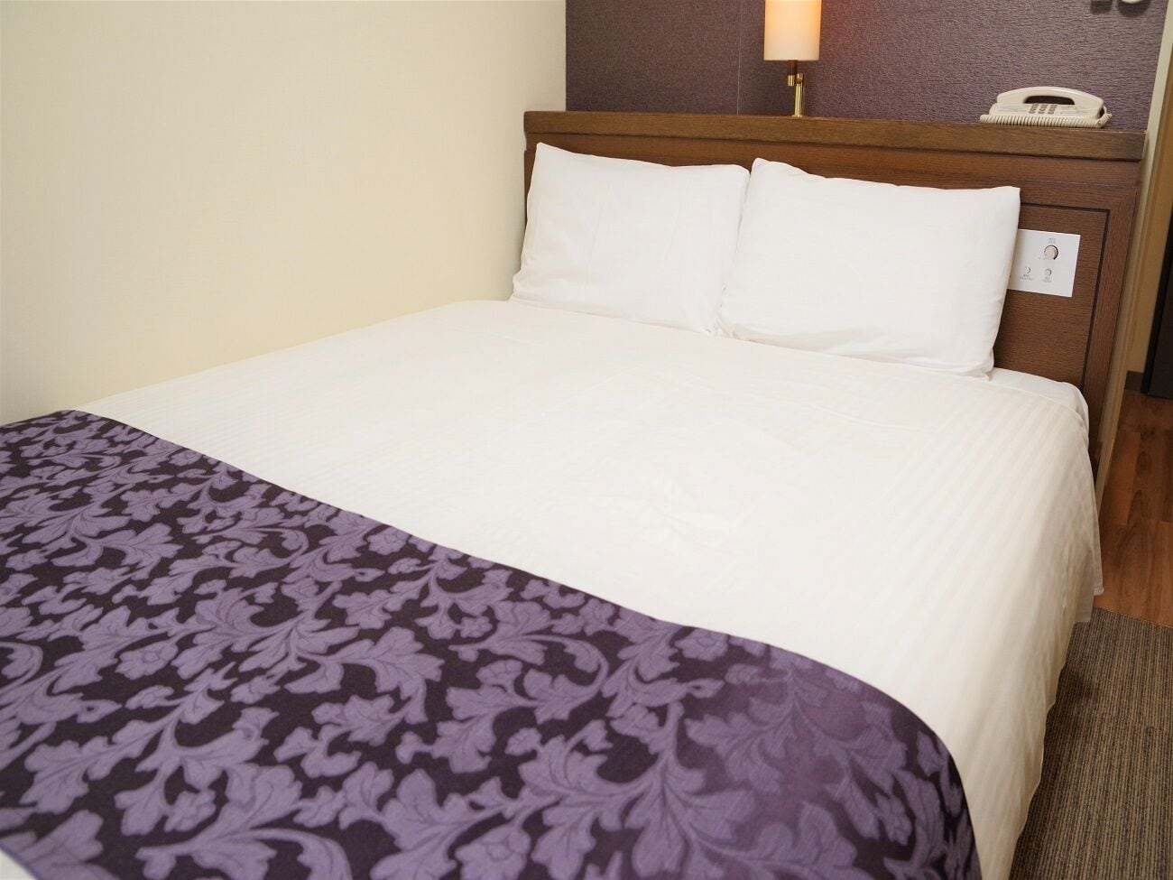 A hotel room with a bed, a telephone, and a wall-mounted light fixture.