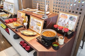 Ein Buffet mit verschiedenen Speisen, darunter ein großer Suppentopf, Schüsseln mit Essen und ein Grill.
