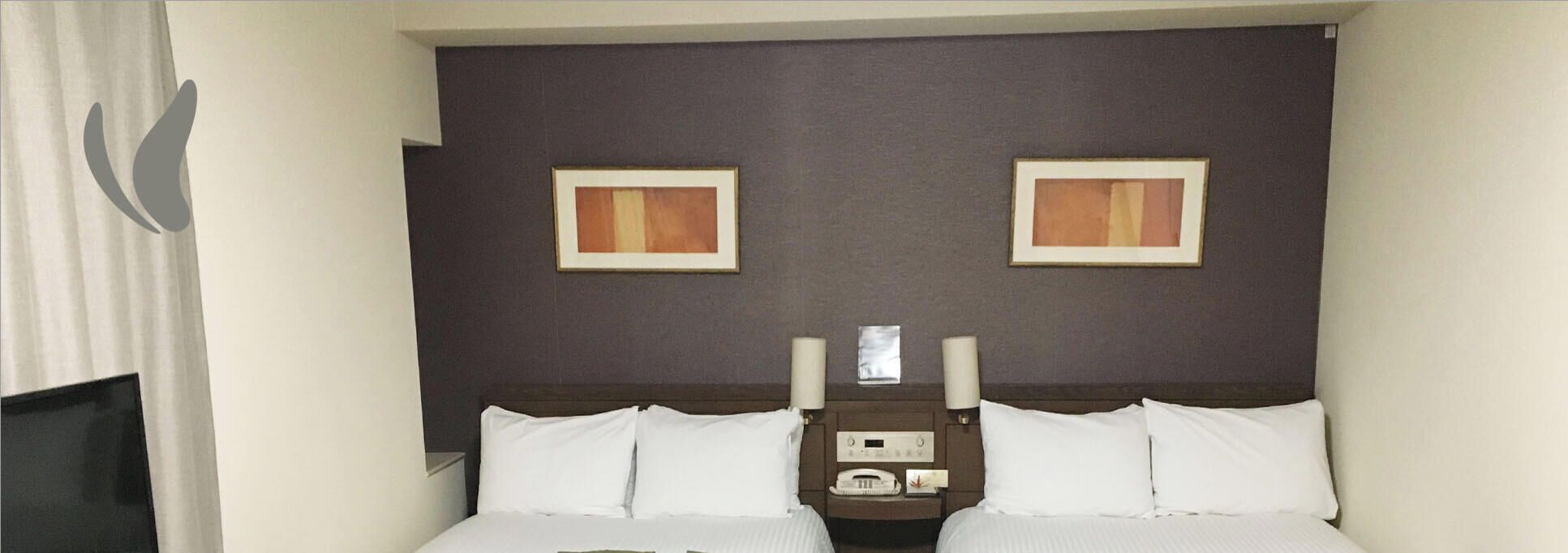 A hotel room with a bed, two bedside tables, a headboard, and two framed pictures on the wall.