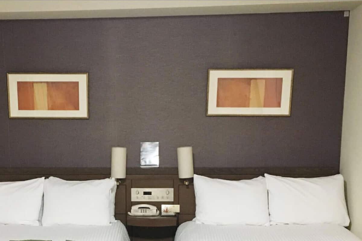 A hotel room with a bed, two bedside tables, a headboard, and two framed pictures on the wall.