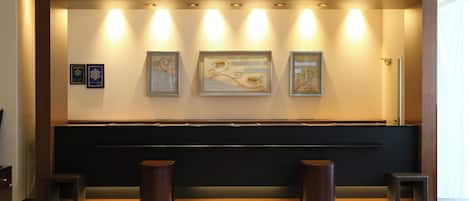 A reception area with a reception desk, framed artwork, and two stools.