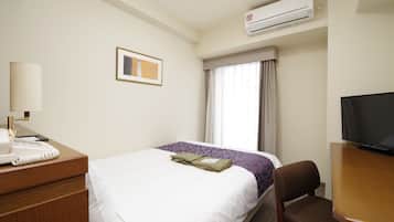 Quarto de hotel com uma cama, uma secretária com telefone, uma cadeira, uma televisão e ar condicionado.