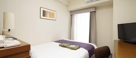 A hotel room with a bed, a desk with a telephone, a chair, a television, and an air conditioning unit.