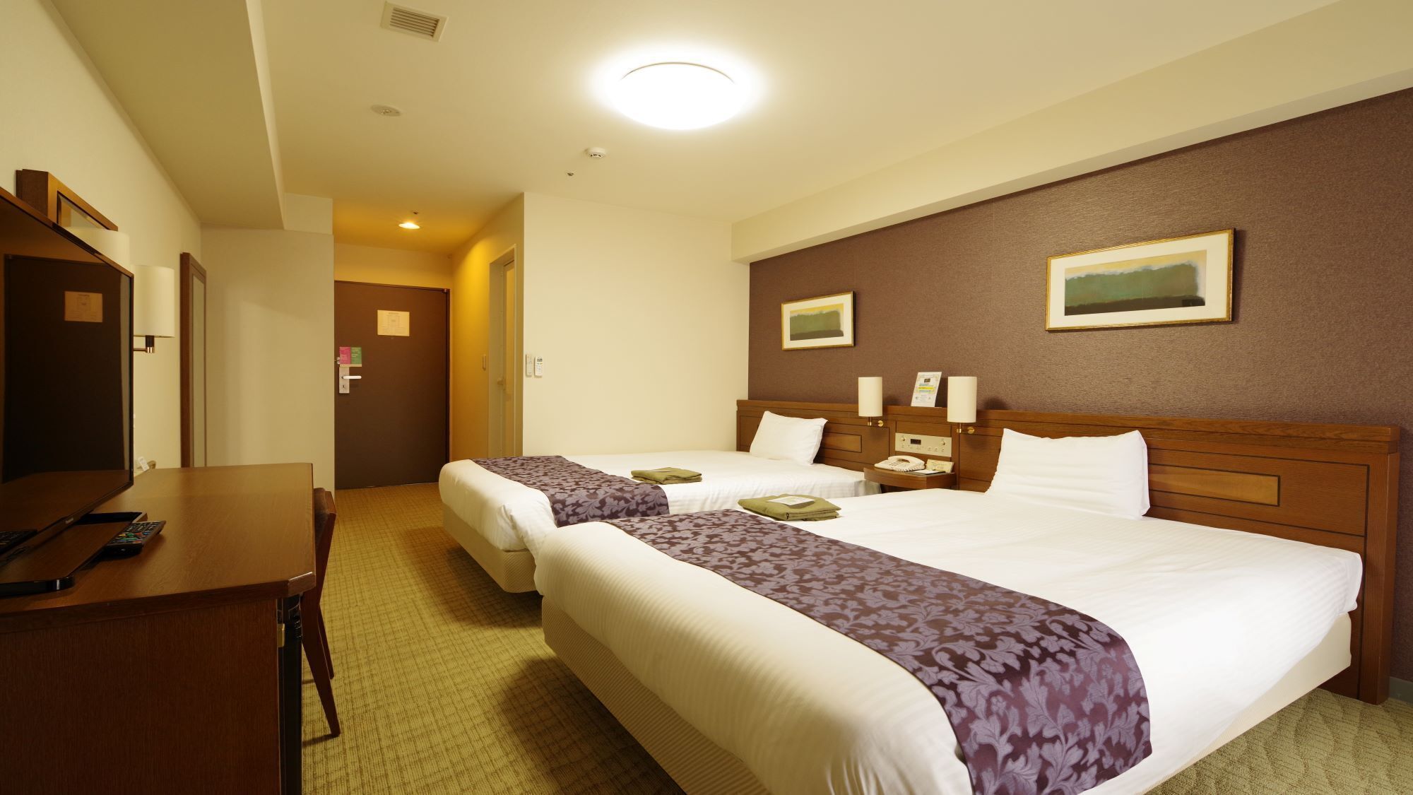 A hotel room with two beds, a desk, and a telephone.