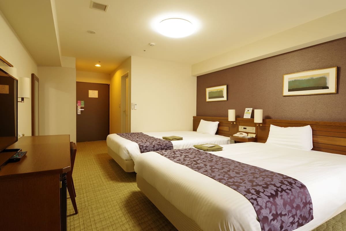 A hotel room with two beds, a desk, and a telephone.