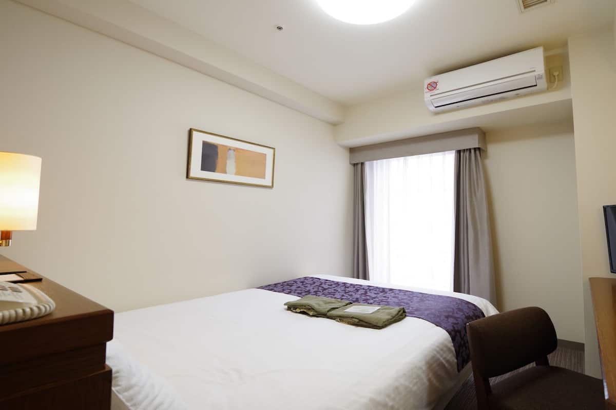 Et hotelværelse med en seng, et skrivebord med lampe, et fjernsyn og en aircondition.