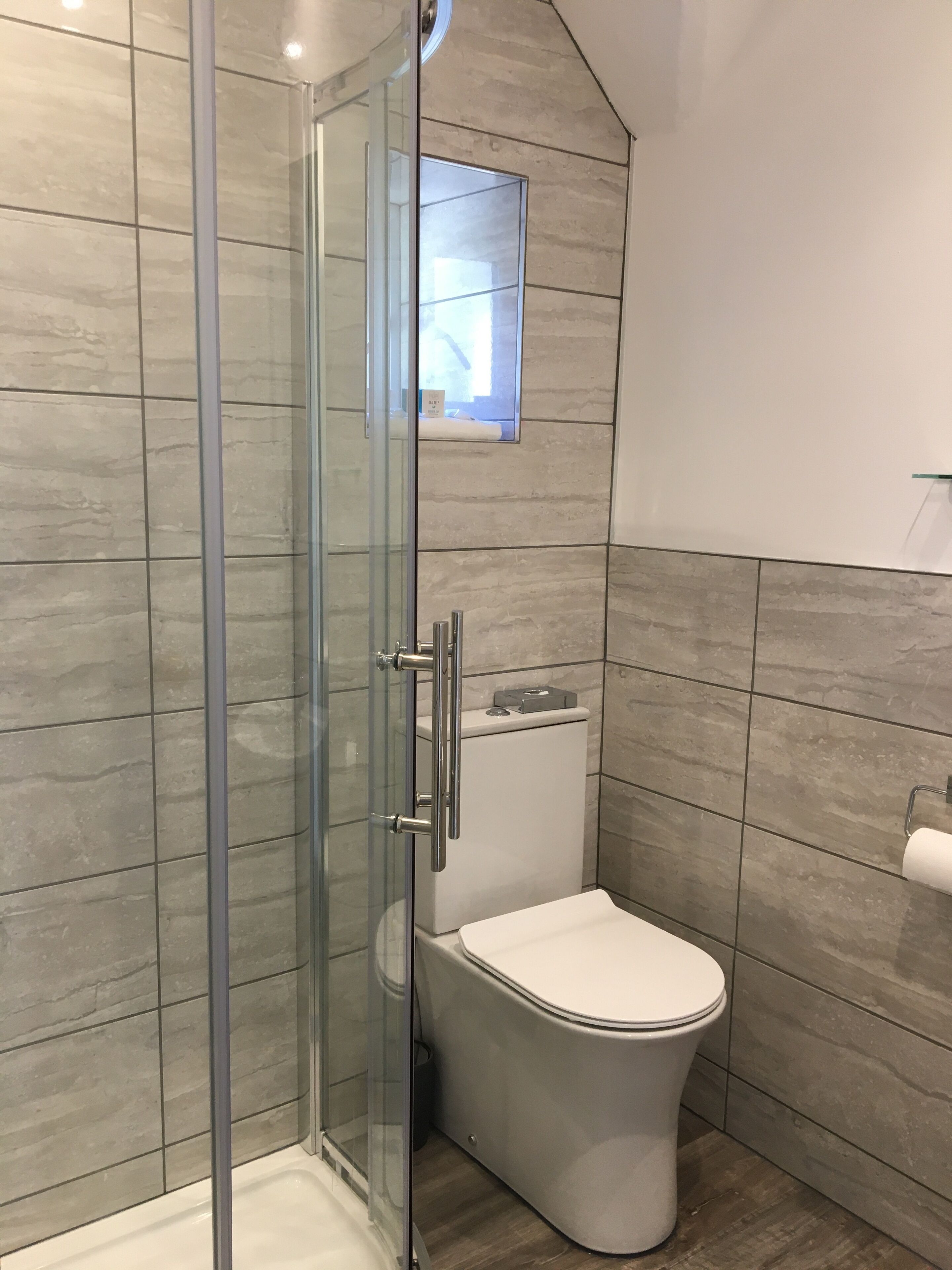 Une salle de bain moderne avec une douche à parois de verre, des toilettes et une petite fenêtre située au-dessus des toilettes.