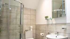 Un baño moderno con ducha de vidrio, inodoro y lavamanos con espejo.